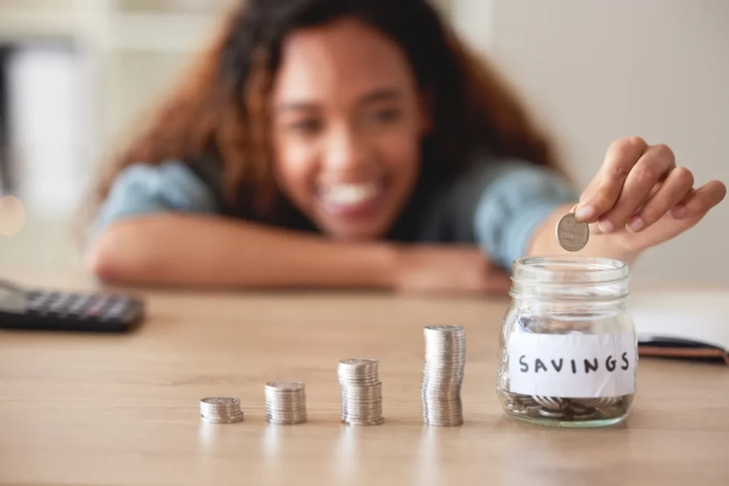Saving Made Difficult but Not Impossible (woman placing coins into a jar with a "savings" label)