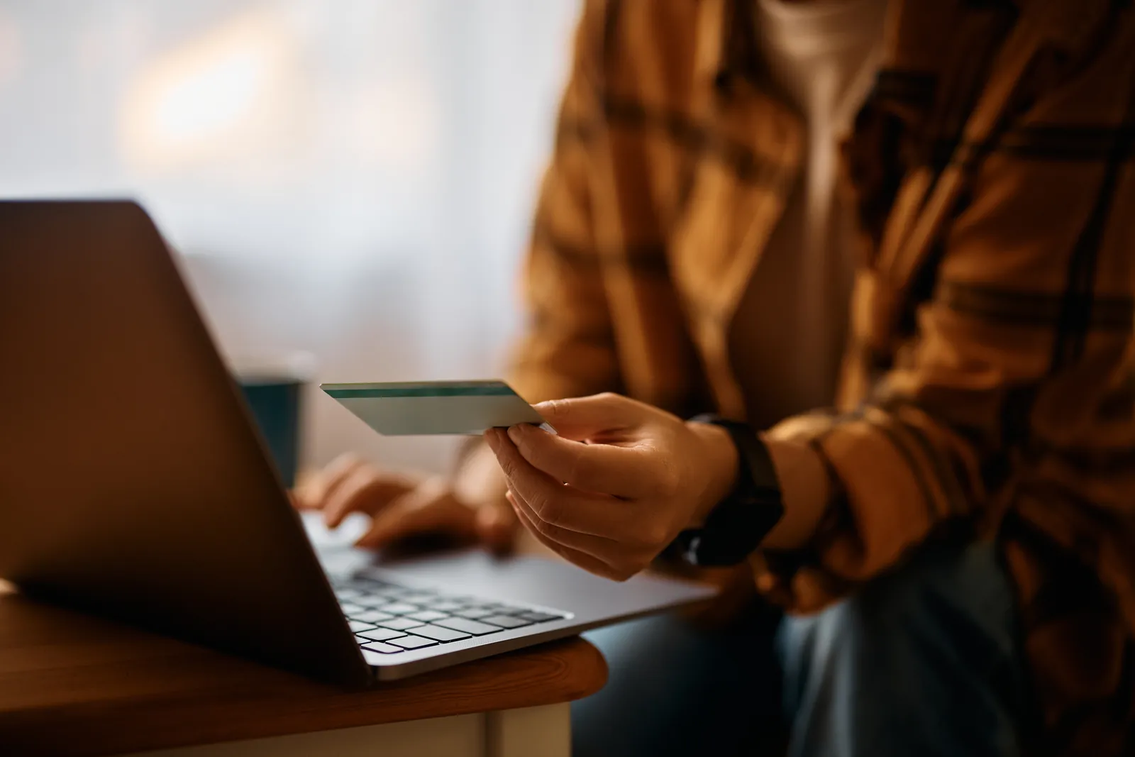 Financial Risks of Extended Black Friday (Person holding up and reading a bank card while working on their laptop)